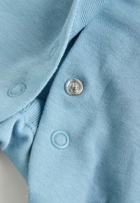 Light blue fabric with a soft, textured surface features a silver snap button and a matching blue button for closure.