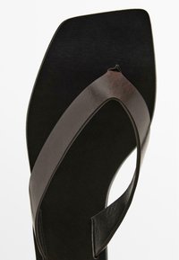 Black leather ankle strap sandal with a smooth texture, wide toe strap, and a square-shaped footbed, featuring minimalistic design details.