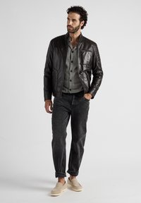 Brun läderjacka med en strukturerad design och texturerade axlar, i kombination med en grå skjorta och mörka jeans. Avslappnade skor fulländar looken.