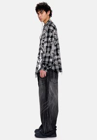 Μακρυμάνικο πουκάμισο με ασπρόμαυρο καρό σχέδιο και φθαρμένες άκρες, σε συνδυασμό με σκουρόχρωμο, υφασμάτινο oversized παντελόνι και μαύρα παπούτσια.