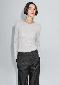 Grijze lange mouw top van gestructureerde tricot, gecombineerd met hoge taille, zwarte wijde broek. Eenvoudig, nauwsluitend design met ronde hals.