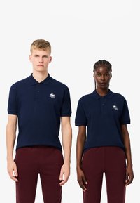Granatowe koszulki polo wykonane z bawełny, z krótkimi rękawami, płaskim kołnierzykiem i małym logo na piersi. Noszone z bordowymi spodniami.