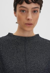 Haut en tissu texturé bleu marine avec un col rond, présentant un motif subtil et une couture centrale. Le matériau semble doux et léger.