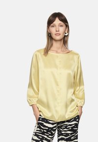 Yellow satin blouse with three-quarter sleeves, rounded neckline, and elastic cuffs, paired with black and white zebra-print trousers.