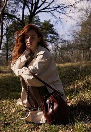Braune Leder-Eimer-Tasche mit einer Kordelzugverschluss und runden Akzenten. Glatte Textur, kompakte Form, als Crossbody-Tasche mit einem Tragriemen getragen.
