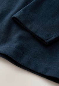 Sötétkék pamut póló anyag, sima textúrával, meghajtott ujjal és tiszta, diszkrét varrással készült szegéllyel.