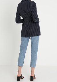 Námořnický pruhovaný dlouhý blazer s páskem v pase, nošený přes světle modré rovné džíny a černé sandály na blokovém podpatku.