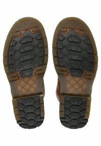 Podrážky hnědých kožených bot s černým a průhledným hnědým gumovým vzorkem s geometrickými vzory a logem "Dr. Martens Air Cushion Sole".