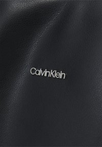 Cuir noir texturé avec un logo "CalvinKlein" argenté en relief, mettant en valeur des motifs lisses et subtils dans le matériau.