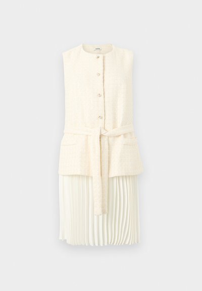 Αμάνικο εκρού γιλέκο με υφή, μπροστινά κουμπιά, ζώνη, δύο τσέπες, πάνω από λευκή πλισέ midi φούστα, παρουσιασμένο σε λευκό φόντο.