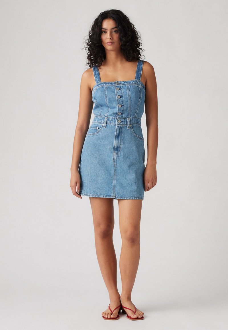 Denimkleit ruudukujulise kaeluse, reguleeritavate rihmade, ees olevate nööpide ja kinnise vöökohtadega, mis üleminekul avardub seelikuosa, helesinises värvitoonis.