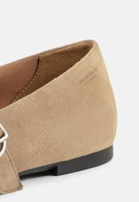 Beżowe zamszowe płaskie buty z okrągłym czubkiem, czarną gumową podeszwą i srebrnym zapięciem po boku. Gładka tekstura i minimalistyczny design.