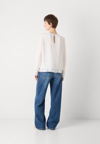 Lichtgewicht, sheer crème blouse met lange mouwen en kantaccenten bij de manchet. Voorzien van een kleine sleutelgatopening aan de achterkant. Gekocht in combinatie met wijd uitlopende denim jeans.