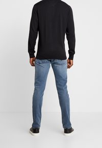 Maglietta nera a maniche lunghe e jeans in denim azzurro chiaro con vestibilità slim. La maglietta è dotata di un collo rotondo e polsini testurizzati; i jeans hanno tasche posteriori.