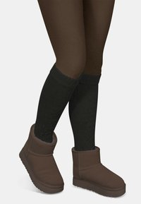 Braune Knöchelstiefel aus weichem Stoff, mit einer dicken Sohle und Innenfutter. Kombiniert mit schwarzen, strukturierten kniehohen Socken.