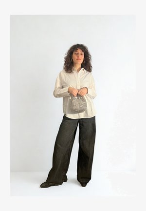 Witte lange mouwen blouse met een knop-down kraag, gecombineerd met zwarte wijde broekspijpen. Houdt een kleine, patroon handtas vast.