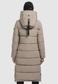 Beige pufferjack met een lang ontwerp, horizontaal gestikte secties, een grote kap en zijritsen. Materiaal lijkt glad en waterafstotend.