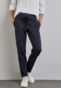 Navy joggers with a drawstring waist, side pockets, and tapered legs, made from a soft material, paired with white sneakers.