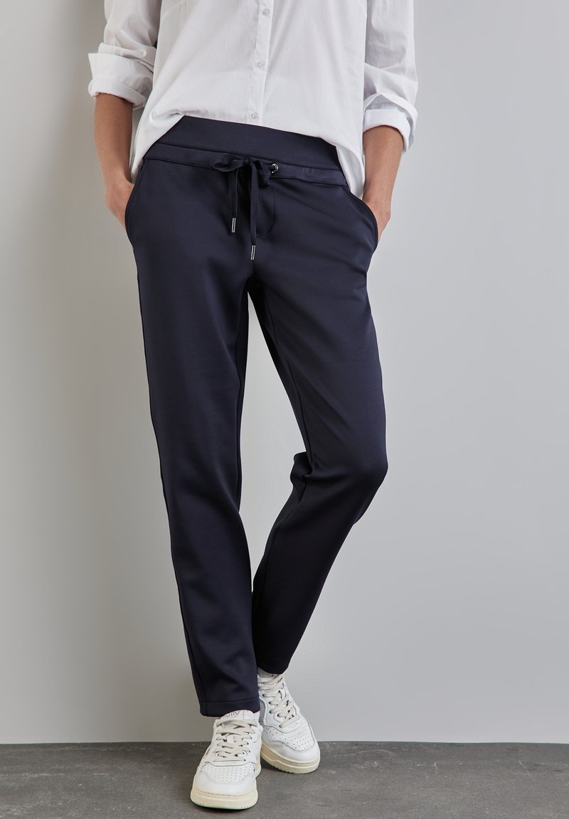 Navy joggers with a drawstring waist, side pockets, and tapered legs, made from a soft material, paired with white sneakers.