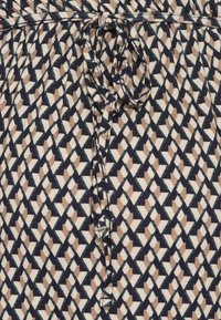 Tejido beige con un patrón geométrico en azul marino, con cordón en la cintura y detalles de superficie texturizada.