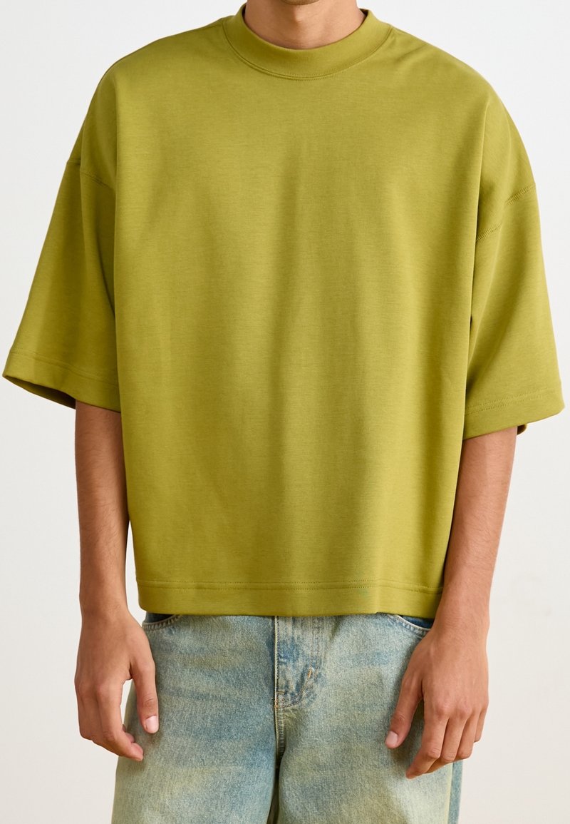 Olivgrön oversized t-shirt med korta ärmar och rundad halsringning, gjord av mjuk väv, ihopparad med ljusblå denimshorts.