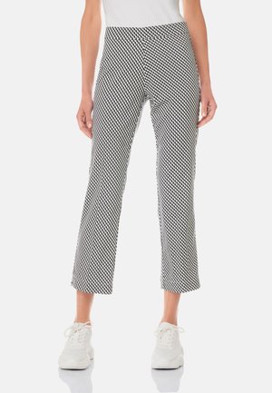 Mujer con pantalones cortos de estampado geométrico en blanco y negro, zapatillas blancas y una camiseta blanca, de pie sobre un fondo blanco.