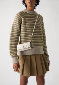 Prúžkovaný sveter v žltej, sivej a krémovej farbe, s rebrovanými manžetami. V páre s béžovou skladanou sukňou a bielou crossbody taškou s vzorovaným dizajnom.
