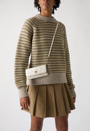 Maglione a righe giallo, grigio e crema, con polsini a coste. Abbinato a una gonna plissettata beige e una borsa a tracolla bianca con un design a motivi.