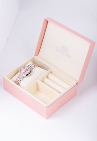 Sudraba un rozā zelta pulkstenis ar apaļu ciparnīcu rozā tekstūrētā kastē, kas iekšpusē izklāta ar krēmkrāsas audumu; ietver nodalījumus papildu priekšmetiem.