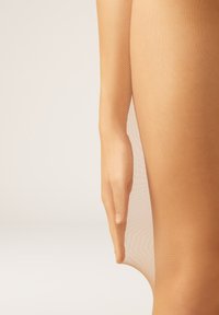 Beige transparente Strumpfhosen mit glatter Textur, mit einer Nahaufnahme einer Hand, die den seitlichen Bereich des Beins hält und die Transparenz hervorhebt.