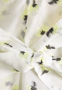 Tissu blanc transparent avec des motifs floraux jaunes et noirs ; noué au centre ; léger et texturé. Convient aux temps chauds.