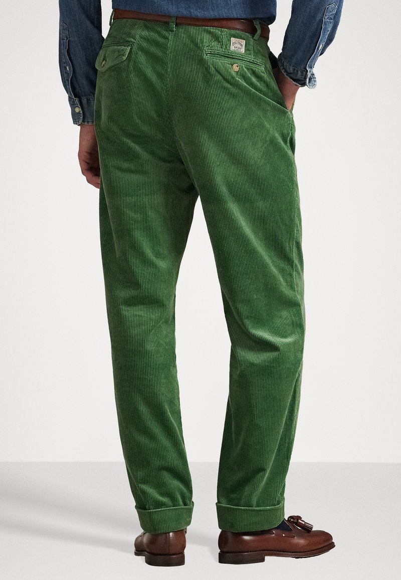 Green corduroy pants with vertical ribbed texture, back pockets, and a rolled hem. Paired with brown leather shoes.