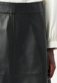 Schwarzer Lederrock mit glatter Textur, hohem Bund und horizontaler Nahtdetail. Der Stoff wirkt weich und flexibel.