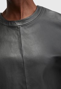 Top in pelle nera con scollo rotondo, texture liscia e dettagli delle cuciture sottili sul davanti. La vista ravvicinata mette in risalto la qualità del tessuto.
