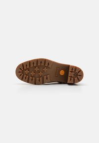 Semelle en caoutchouc brun avec un motif de dentelure texturé, comprenant des designs hexagonaux et en croix. Comprend le logo Timberland sur le côté.