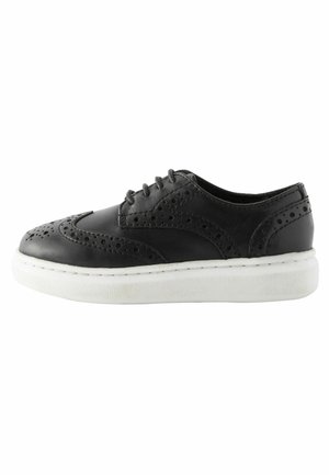 Chaussure en cuir noire avec des détails en brogue, bout rond et semelle épaisse blanche. Dispose de six œillets pour les lacets et d'accents texturés sur la tige.