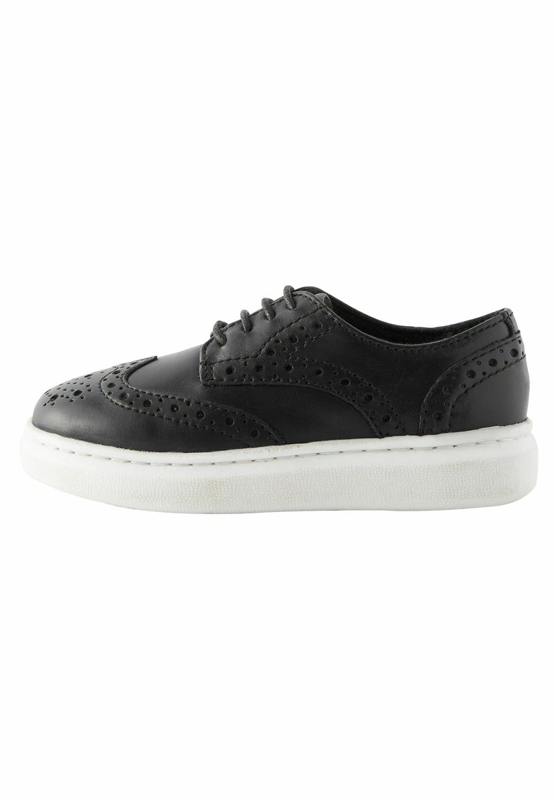 Zapato de cuero negro con detalles de brogue, punta redonda y suela gruesa blanca. Cuenta con seis ojales para los cordones y acentos texturizados en la parte superior.