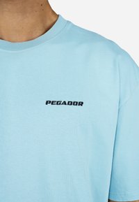 Ανοιχτό μπλε βαμβακερό t-shirt με στρογγυλή λαιμόκοψη και κοντά μανίκια, φέρει τη λέξη "PEGADOR" σε μαύρη κεντημένη γραφή στο στήθος.