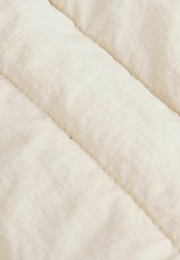 Vadderat tyg i off-white färg med en slät textur, synliga sömmar och ett mjukt, lätt utseende.