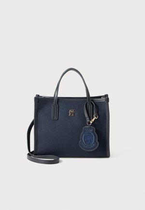 Navy tote bag made of sturdy fabric with dual handles, a detachable shoulder strap, and a blue badge logo accent. Features a simple, structured design.