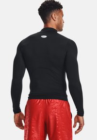 Chemise de sport noire à manches longues avec col haut et design ajusté, associée à un short rouge brillant. Logo centré au dos.
