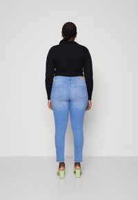 Blå denim skinny jeans med hög midja och en urtvättad finish, kombinerat med en svart topp och gröna klacksandaler. Bakifrån.