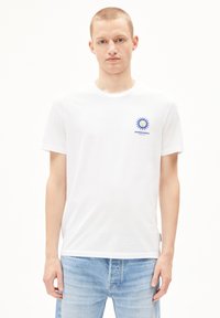 Weißes Baumwoll-T-Shirt mit kurzen Ärmeln, mit einem blauen Sonnenmotiv auf der linken Brust. Lässige Passform mit Rundhalsausschnitt.
