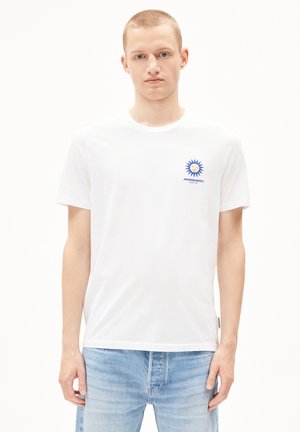 T-shirt en coton blanc à manches courtes, avec un graphique de soleil bleu sur le côté gauche de la poitrine. Coupe décontractée avec un col rond.