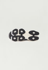 Black rubber outsole with diamond-shaped grip patterns, featuring cream and grey accents. Lightweight and cushioned design for comfort.