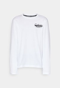 Bílé tričko s dlouhým rukávem vyrobené z bavlny. Na horní levé straně se nachází černé logo Calvin Klein a má kulatý výstřih.