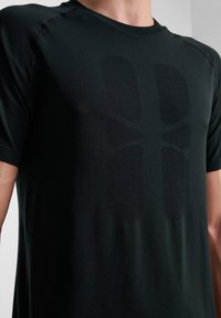 Zwarte sportieve T-shirt gemaakt van gladde stof, met een textuur grafisch ontwerp op de voorkant. Korte mouwen en ronde hals.
