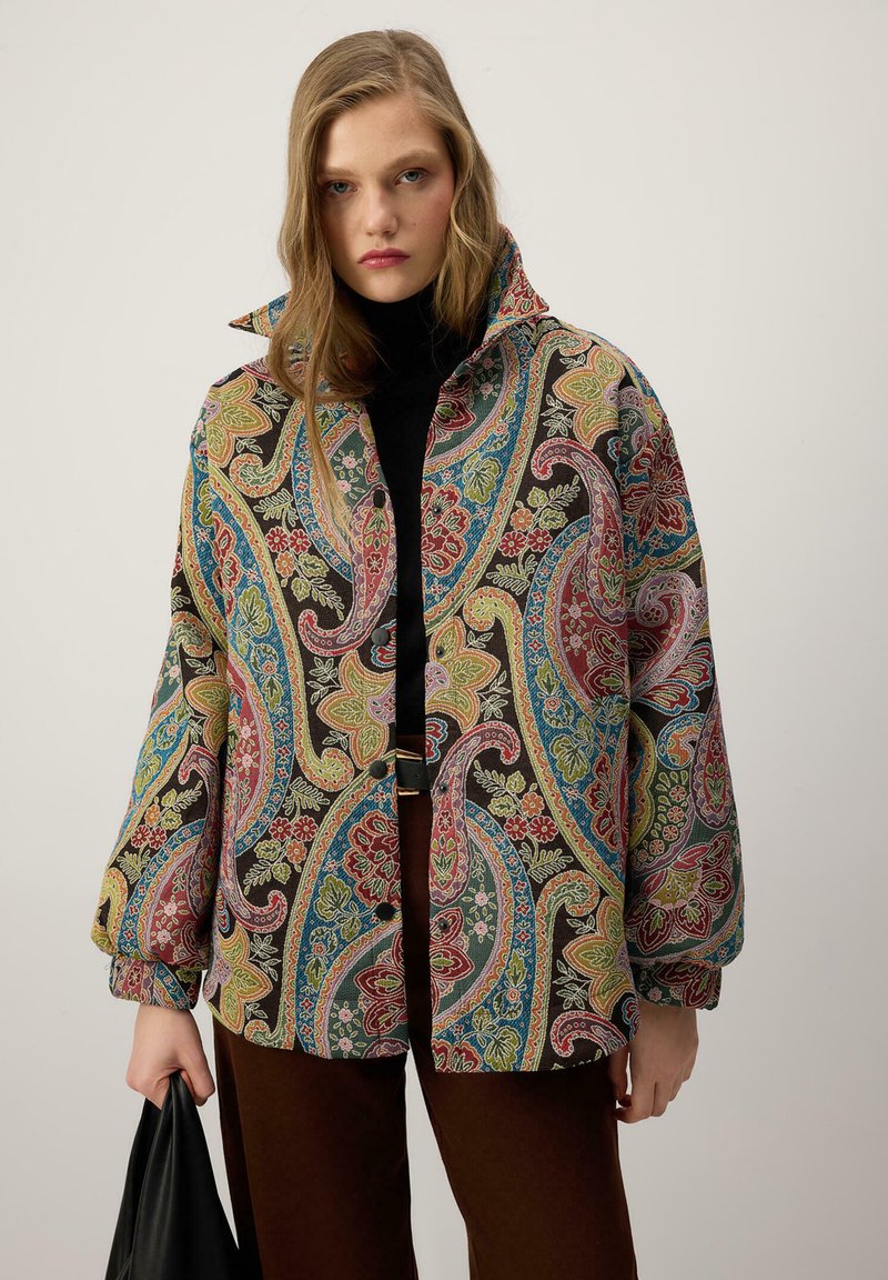 Barvita jakna s paisley vzorcem iz mešanice bombaža, z visokim ovratnikom, zapiranjem na gumbe in sproščenim krojem, kombinirana s temnimi hlačami.