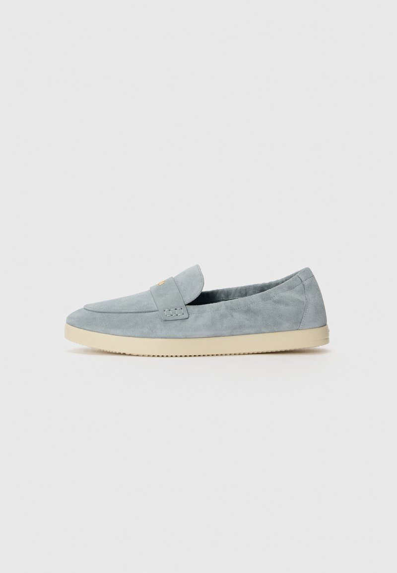 Mocassino in suede blu chiaro con suola piatta in gomma beige, caratterizzato da un accentuato cucitura e un piccolo emblema sul pannello superiore.