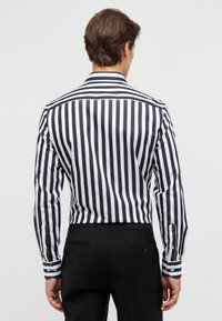 Zwart-wit verticaal gestreept hemd met lange mouwen, een klassieke kraag en contrasterende manchetten. Zwarte broek zichtbaar bij de taille.